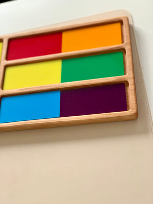 Wooden frame holding six colorful rectangular blocks paired side-by-side in red, orange, yellow, green, blue, and purple on beige surface