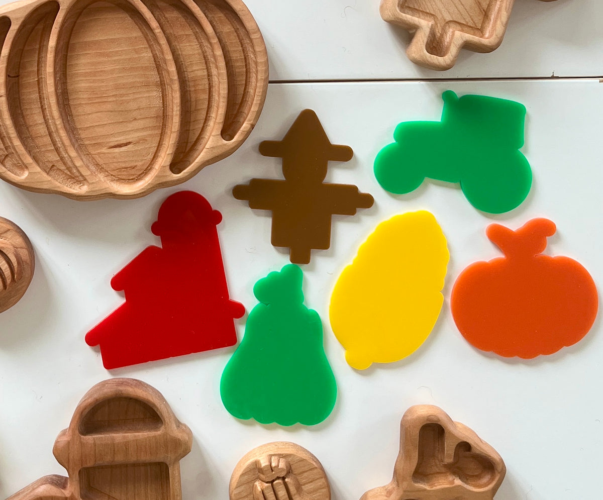 Assorted colorful acrylic farm and harvest shapes including tractor, scarecrow, corn, pumpkin, and barn wooden trays on white surface