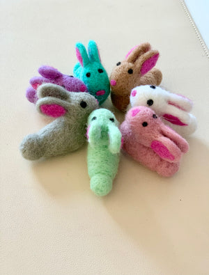 Seven colorful felt bunny finger puppets arranged in a circle on a light surface