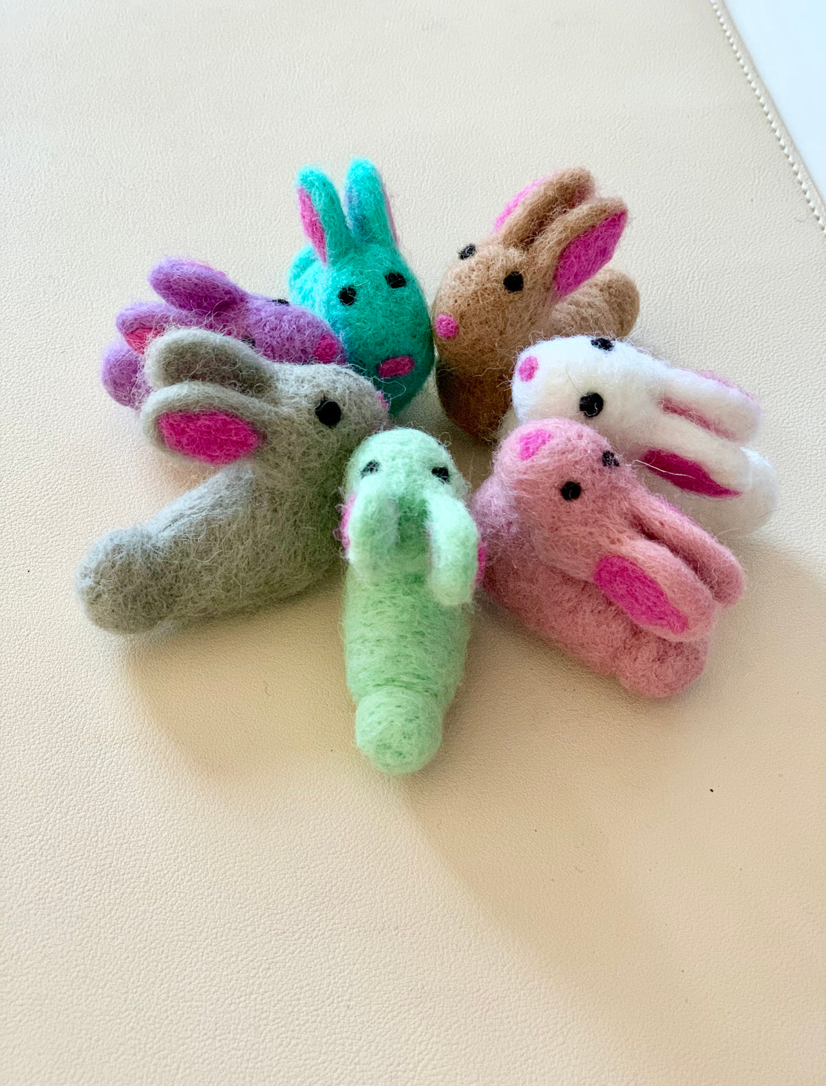 Seven colorful felt bunny finger puppets arranged in a circle on a light surface