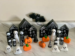 Wooden Halloween peg dolls with ghosts, skeletons, pumpkins, black haunted houses, spider webs, and a flying bat on marble surface