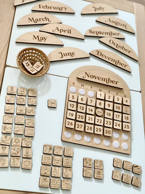 Wooden perpetual calendar with removable month plaques, date tiles arranged under November, and various event icons on white surface