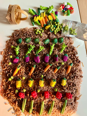 Miniature clay vegetables arranged in rows on textured brown rice with a small woven basket on the side