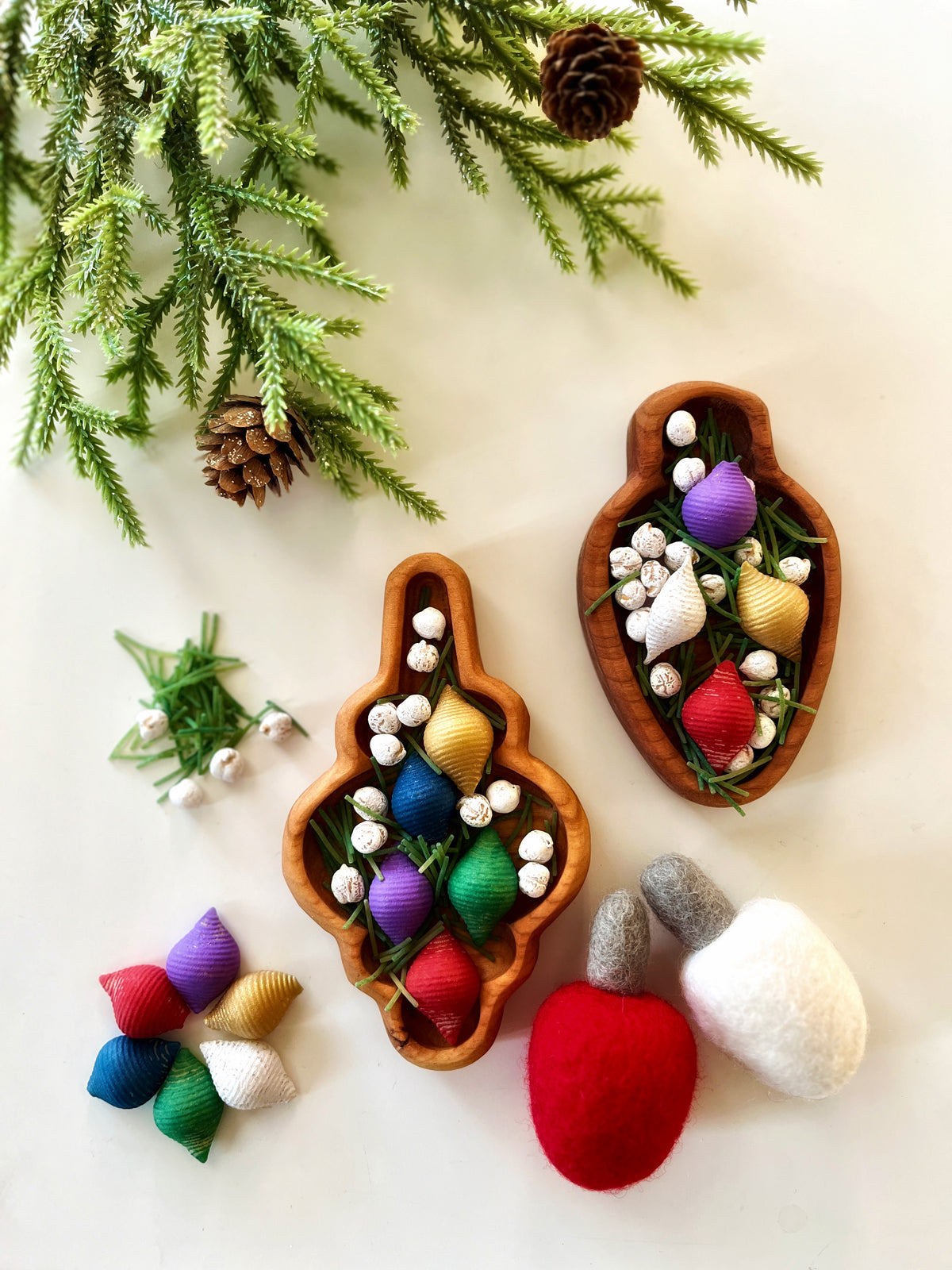 Two wooden trays with colorful shell-shaped ornaments, white berries, greenery, and felt acorns on light background