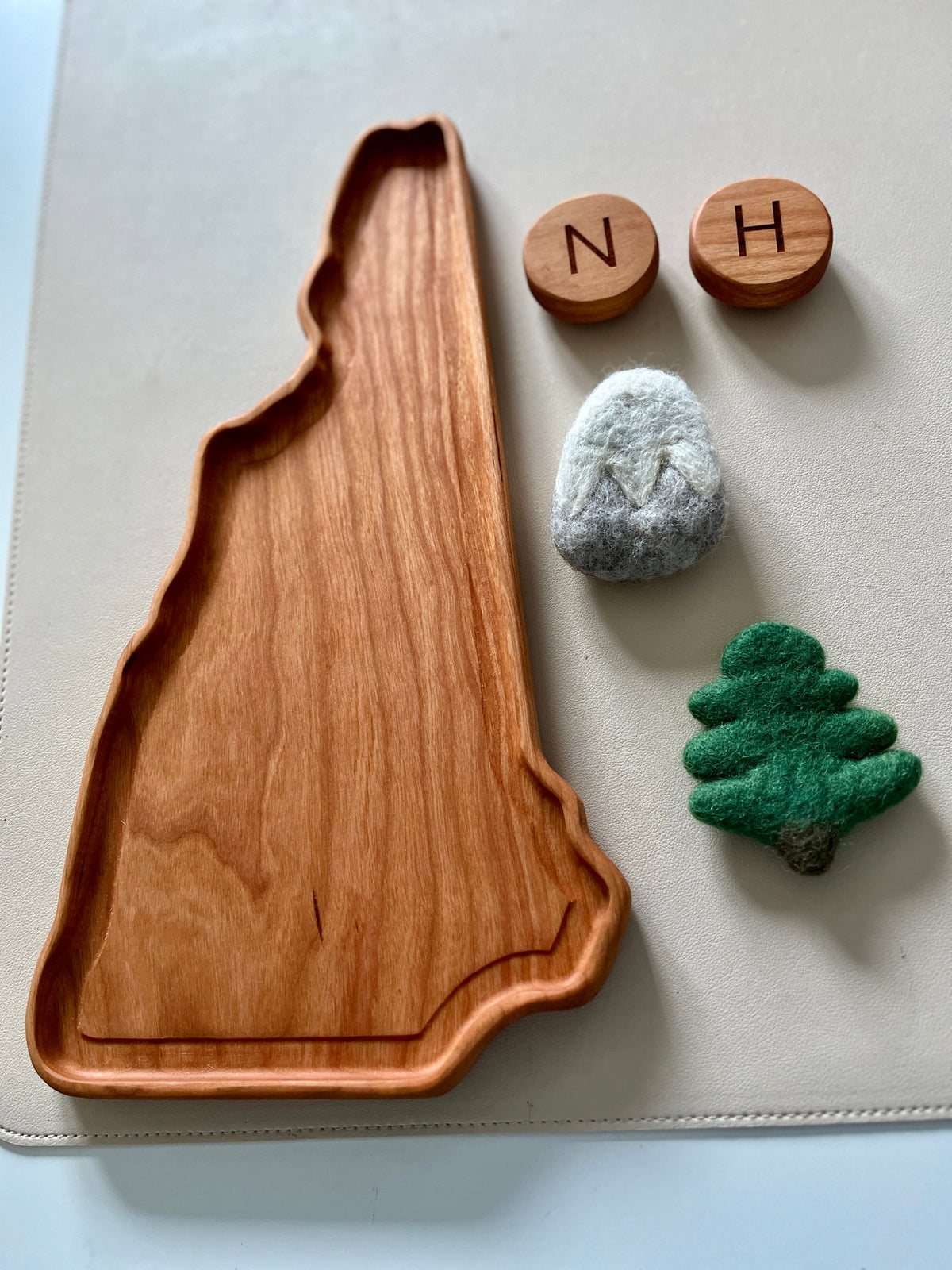 Wooden tray shaped like a state outline alongside two wooden letter tokens and two small felt figures on a light surface