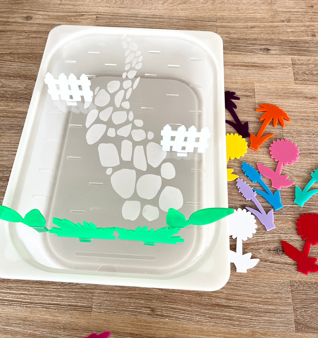 White tray with a stone path and fence design holding colorful acrylic flower-shaped pegs beside it, showcasing STEM Insert – Acrylic Insert with Different Peg Options - Neighborhood, Veggie Garden, Flower Garden, Under the Sea + More, handcrafted, homeschool, education resources.