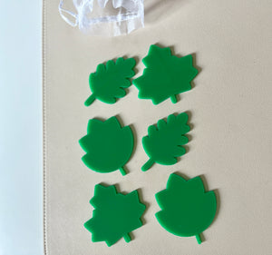 Six bright green plastic leaf-shaped pieces in three distinct designs arranged on a beige surface