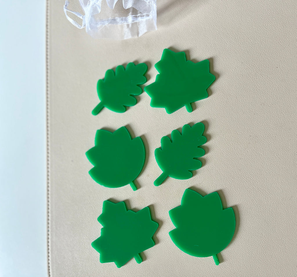 Six bright green plastic leaf-shaped pieces in three distinct designs arranged on a beige surface
