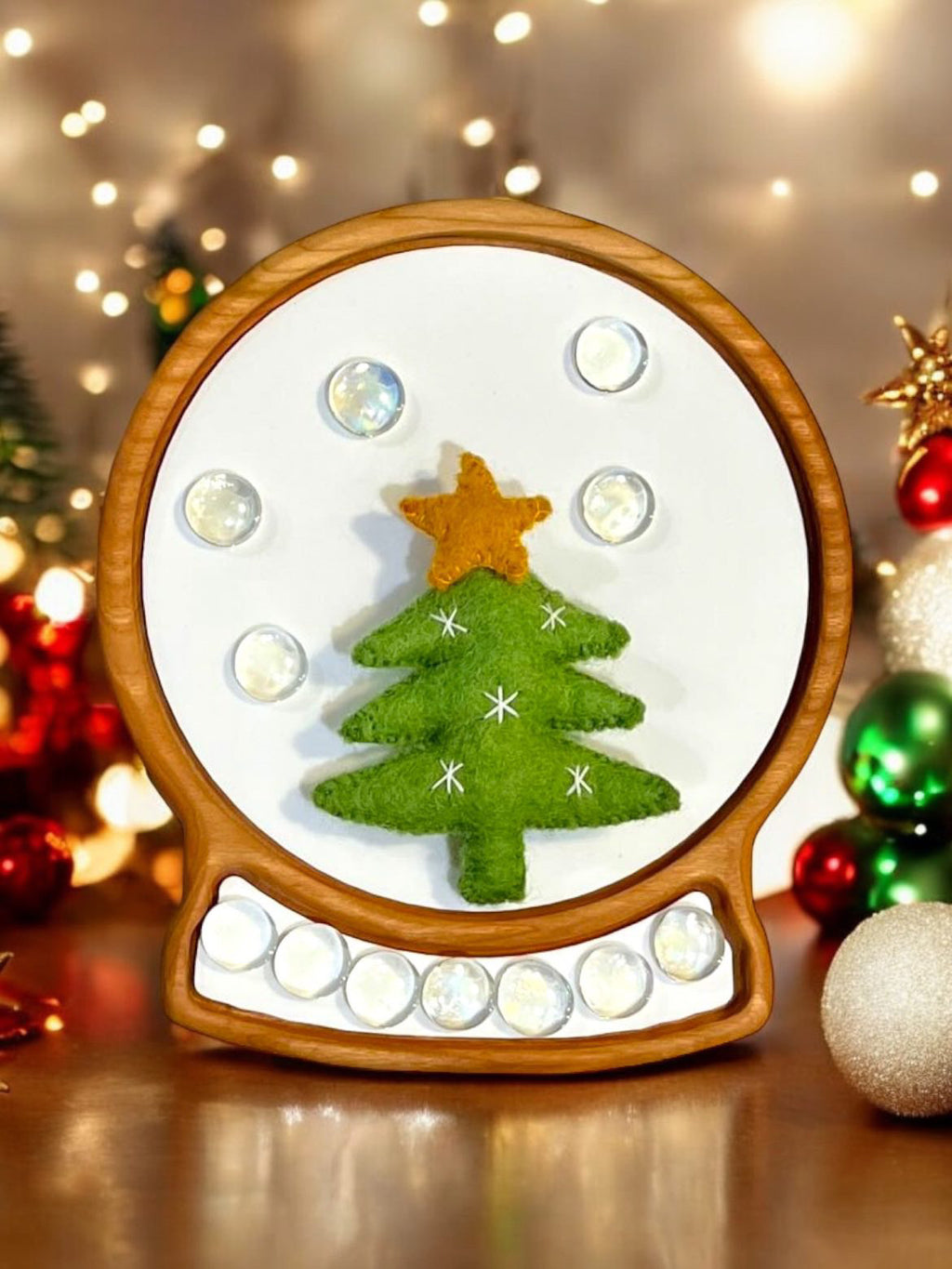 Wooden sensory tray shaped like a snow globe with green felt Christmas tree and clear glass beads on white background