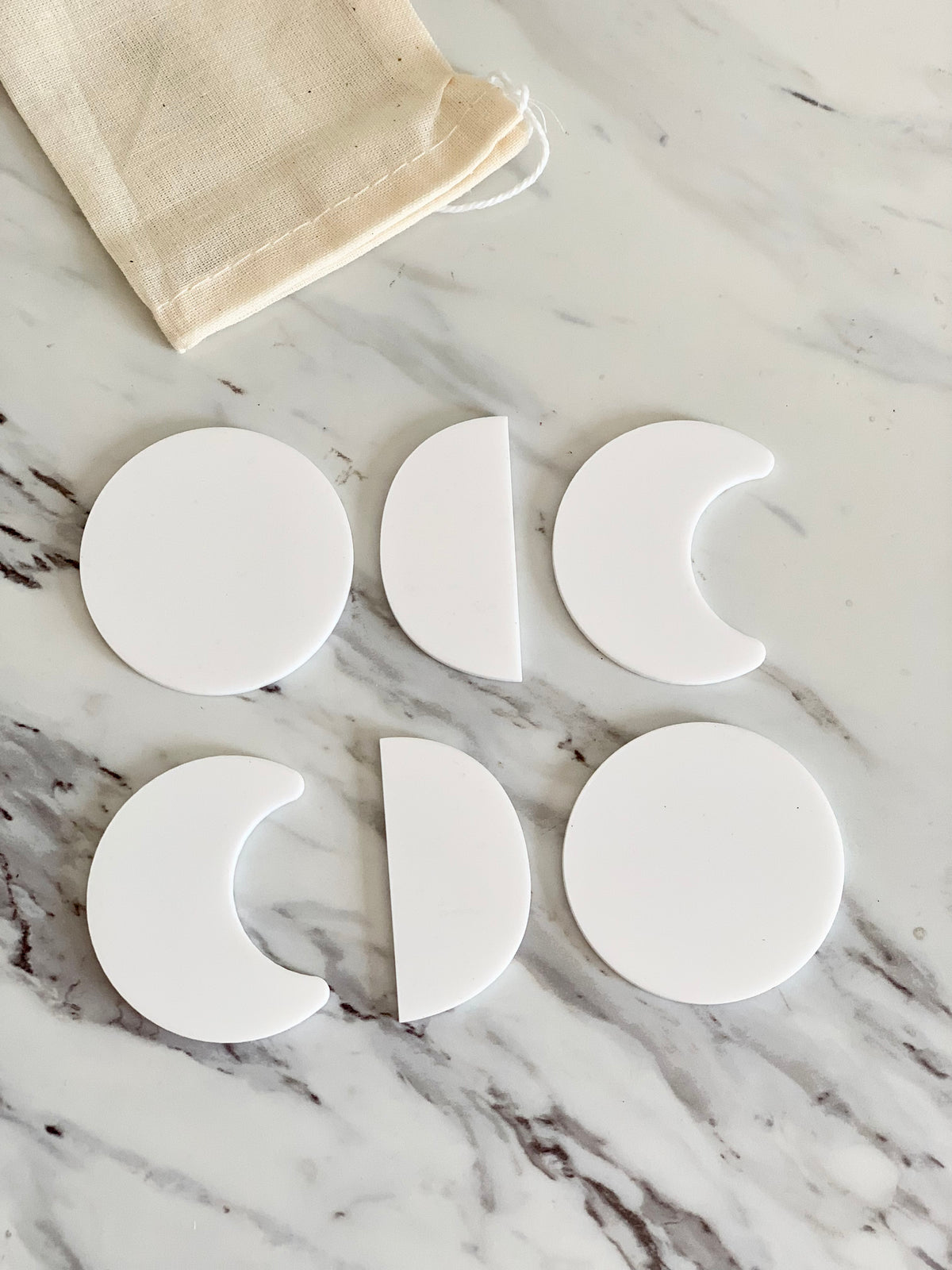 Set of six white dry erasable moon phase shapes arranged on marble surface with beige drawstring pouch nearby