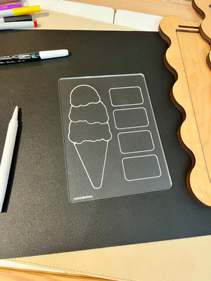 Clear acrylic board with ice cream cone and four rectangular sections on black mat beside white markers and wooden shapes