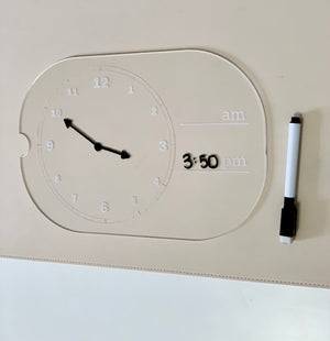 Transparent learning clock with movable hands showing 10:50 and dry erase marker beside 3:50 pm written on it