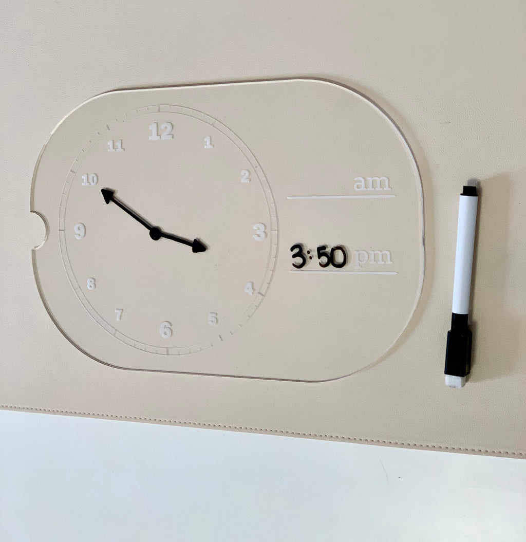 Transparent learning clock with movable hands showing 10:50 and dry erase marker beside 3:50 pm written on it