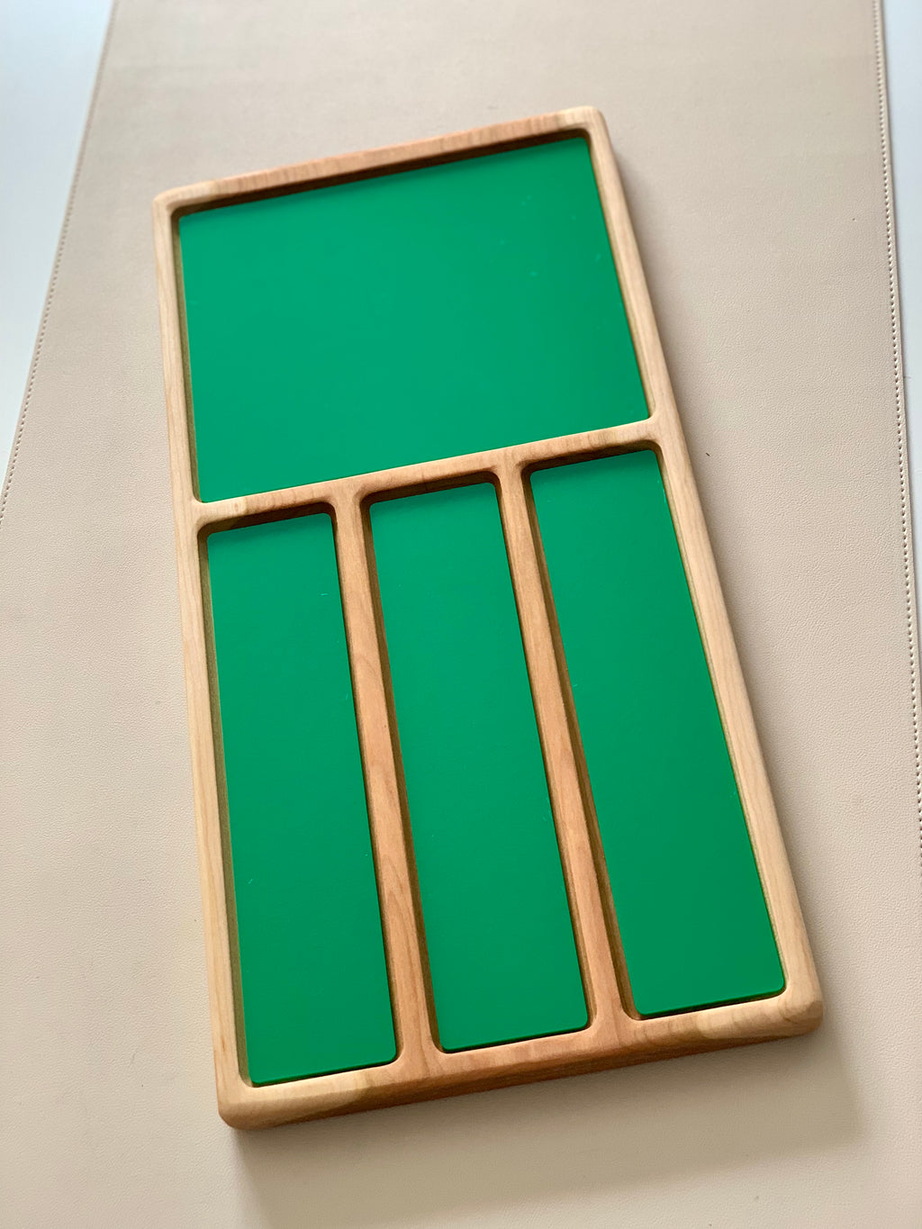 Wooden organizer tray with one large square and three narrow rectangular green panels on a beige surface