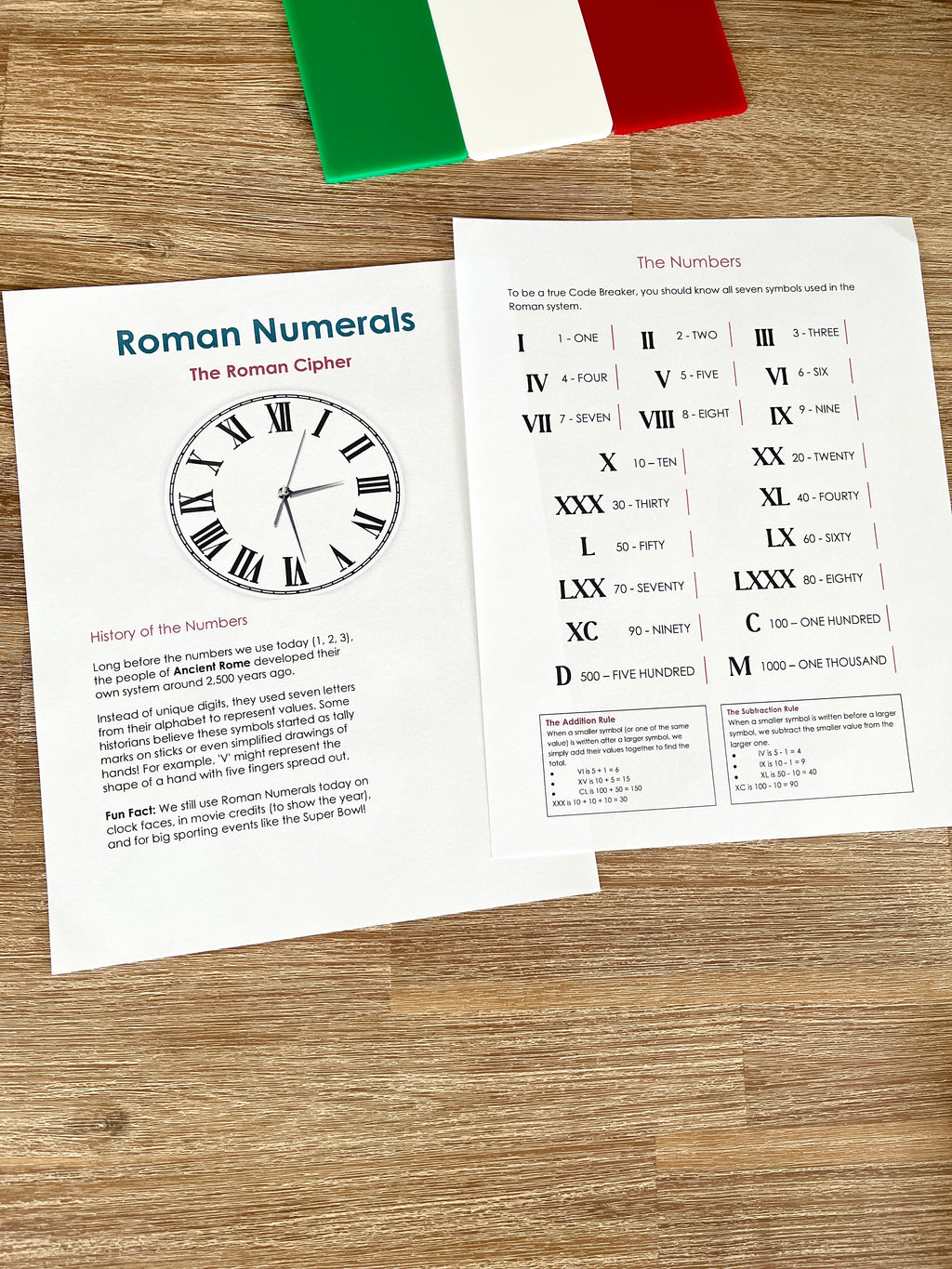Digital Download | Roman Numerals, Their History & DeCoding Activity showing printed educational pages with a Roman numeral clock diagram, numeral charts, and decoding instructions on a wooden surface with an Italian flag decoration, handcrafted homeschool education resources.