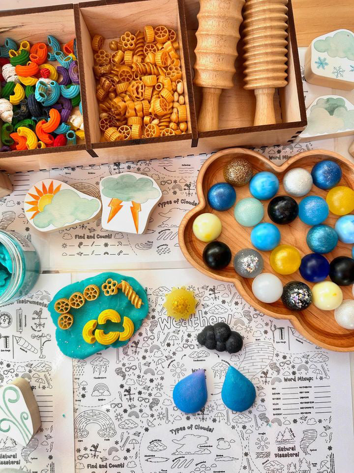 Wooden cloud-shaped sensory tray filled with colorful textured balls on illustrated weather activity mat