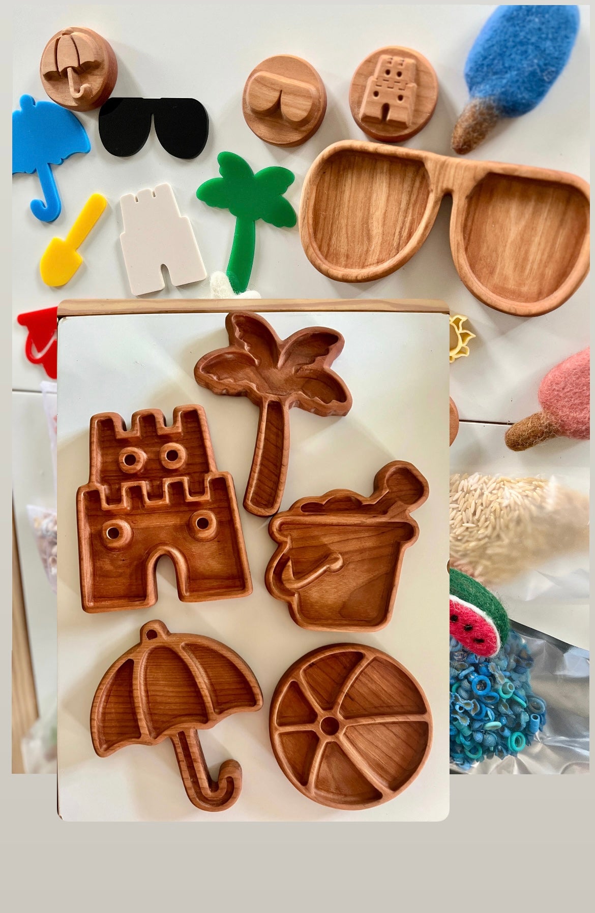 Carved wooden trays shaped like umbrella, palm tree, sandcastle, bucket, and citrus slice surrounded by colorful beach-themed items