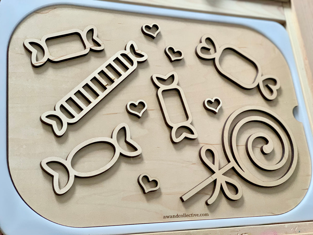 Wooden board with cutout shapes of candies and hearts in various sizes and designs on a white surface