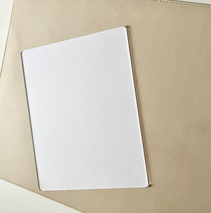 Clear rectangular acrylic or plastic sheet resting on a textured beige surface with soft lighting