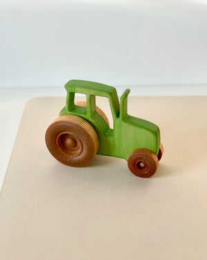 Small green wooden toy tractor with natural wood wheels on a light-colored surface