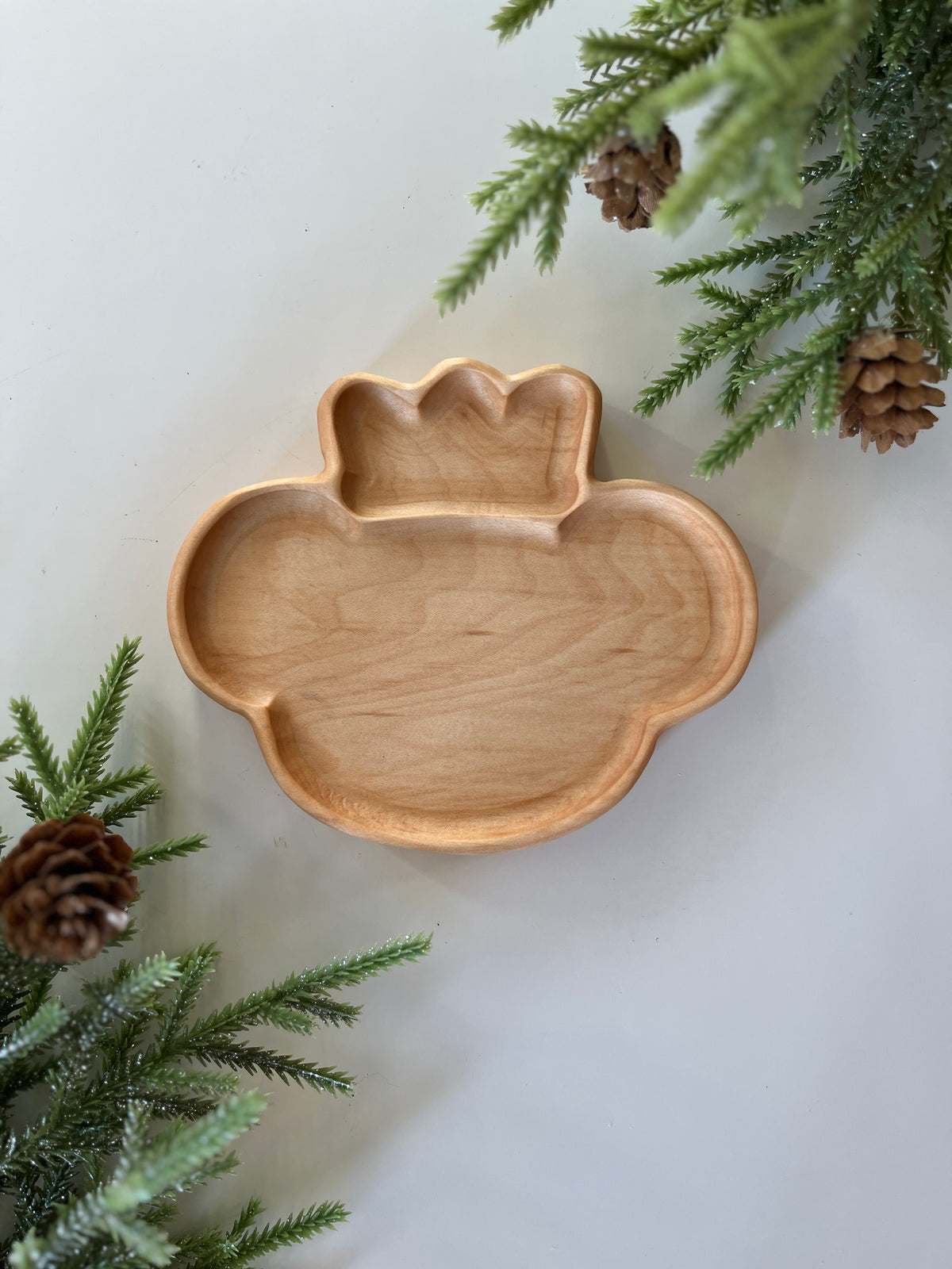 Smooth wooden divided tray shaped like a Christmas ornament with pine branches and cones around it