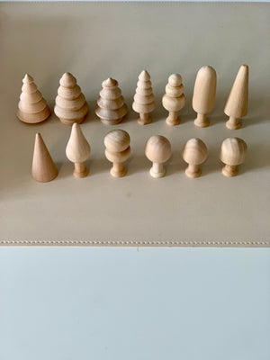 Collection of unfinished natural wooden shapes including cones, spheres, and stylized tree figures arranged on beige surface