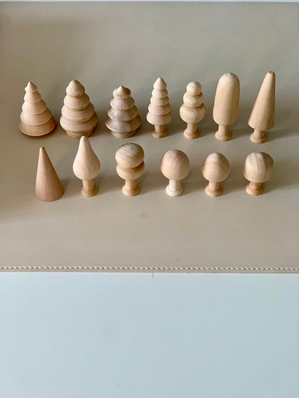 Collection of unfinished natural wooden shapes including cones, spheres, and stylized tree figures arranged on beige surface