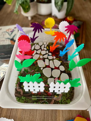 White tray featuring a colorful arrangement of translucent acrylic pegs in various flower and leaf shapes placed along a stone path, showcasing STEM Insert – Acrylic Insert with Different Peg Options - Neighborhood, Veggie Garden, Flower Garden, Under the Sea + More, handcrafted, homeschool, education resources.