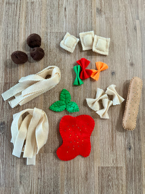 Assorted felt pasta shapes including ravioli, farfalle, noodles, and tomato slice with greens, arranged on a wooden surface, Felt Pasta Set, Made in Canada, handcrafted, homeschool, education resources.