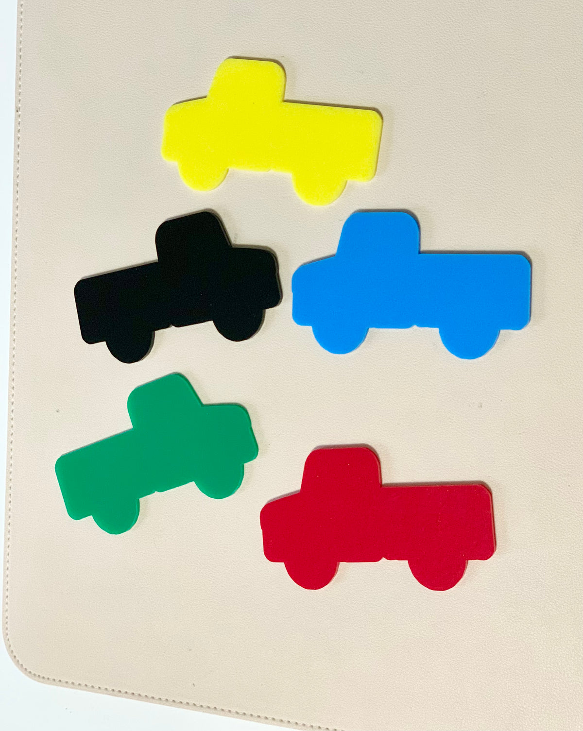 Five flat truck-shaped cutouts in yellow, black, blue, green, and red on a light beige background
