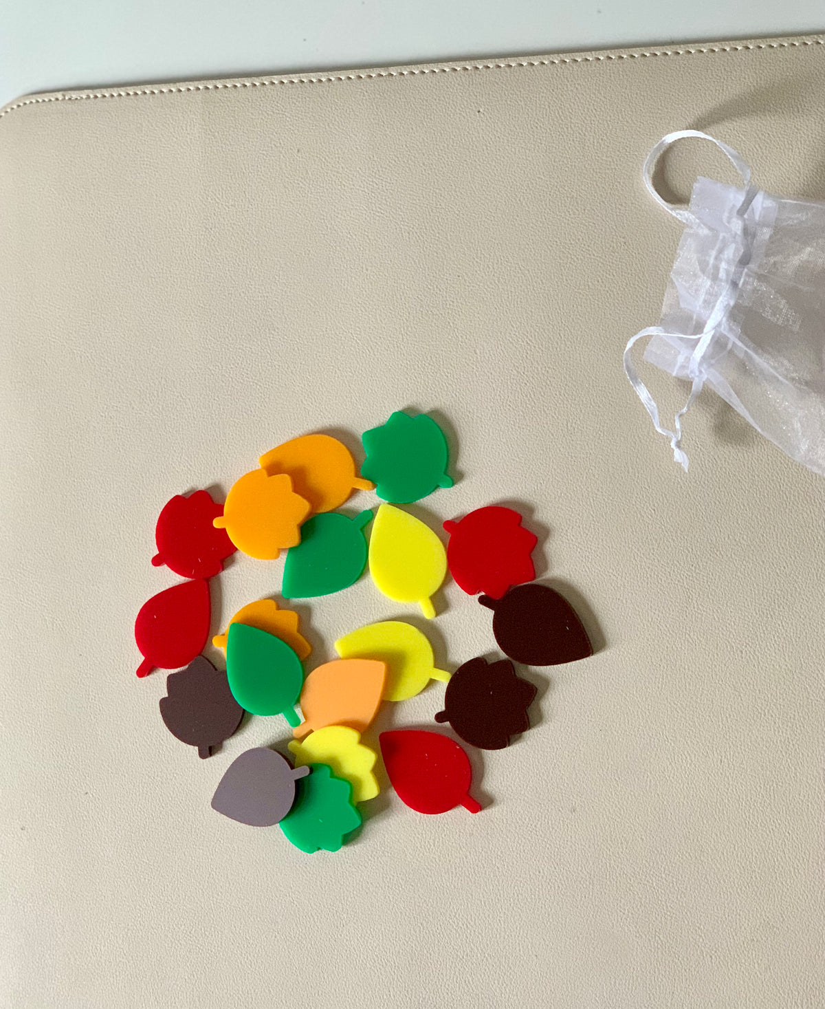 Assorted colorful leaf-shaped tokens scattered near a small white drawstring bag on a beige surface
