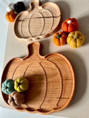 Two carved wooden pumpkin-shaped trays with small colorful felt pumpkins on and around them on a white surface