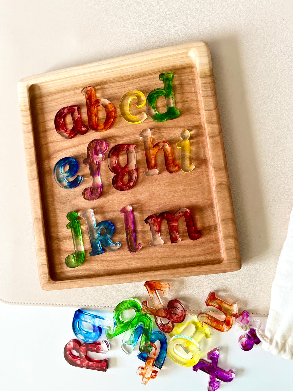 Wooden tray with colorful translucent lowercase alphabet letters arranged from a to m and scattered letters nearby