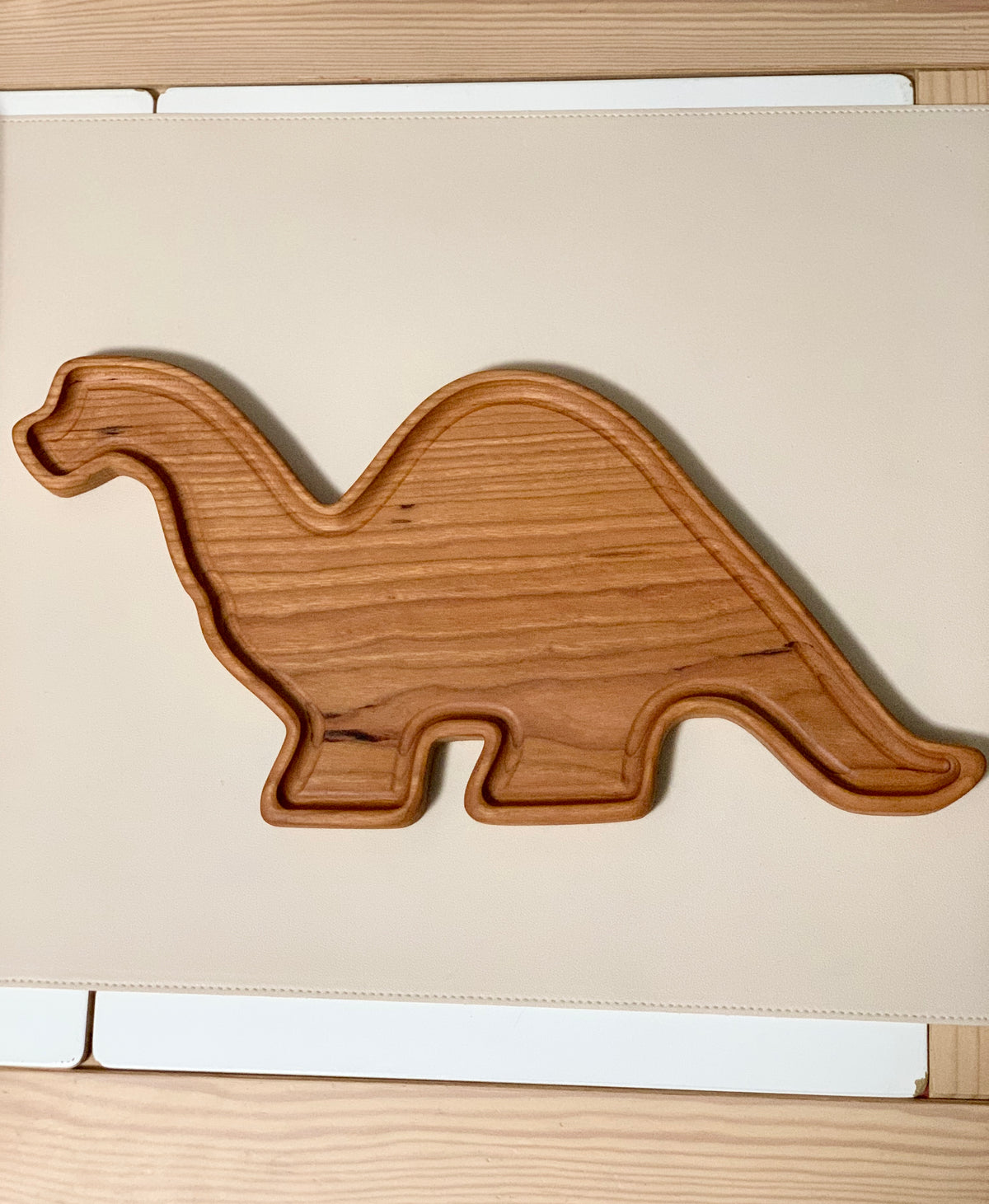 Wooden sensory tray shaped like a Brachiosaurus dinosaur with smooth carved edges on light surface