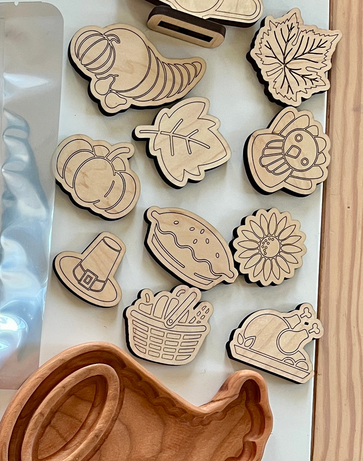 Assorted wooden tokens with Thanksgiving-themed designs including pumpkin, pie, turkey, sunflower, and cornucopia on white surface