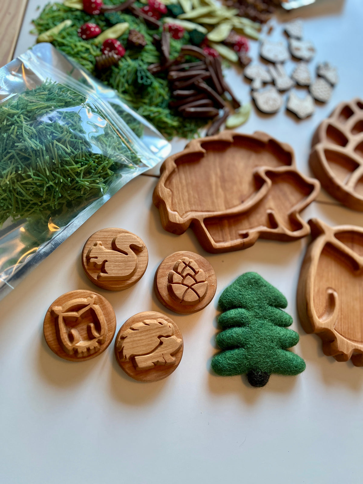 Carved wooden forest-themed stamps, leaf-shaped trays, felt pine tree, and natural green botanicals on white surface