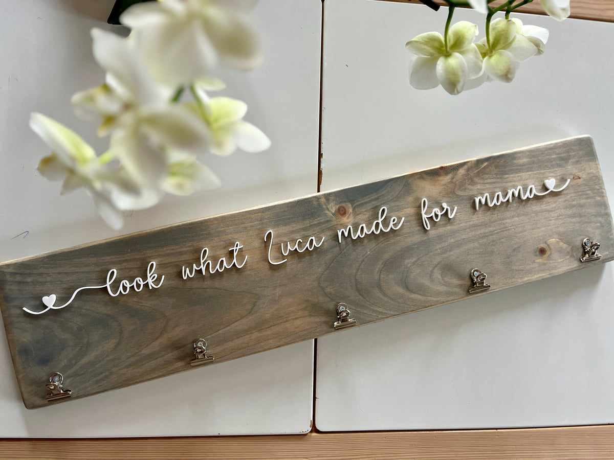 Custom wooden wall sign with white cursive letters reading "look what Luca made for mama" and metal hooks on stained wood