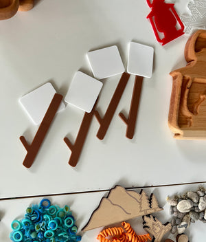 Wooden and plastic play pieces arranged on table including brown branches with white squares, map cutout, blue rings, and orange spiral shapes