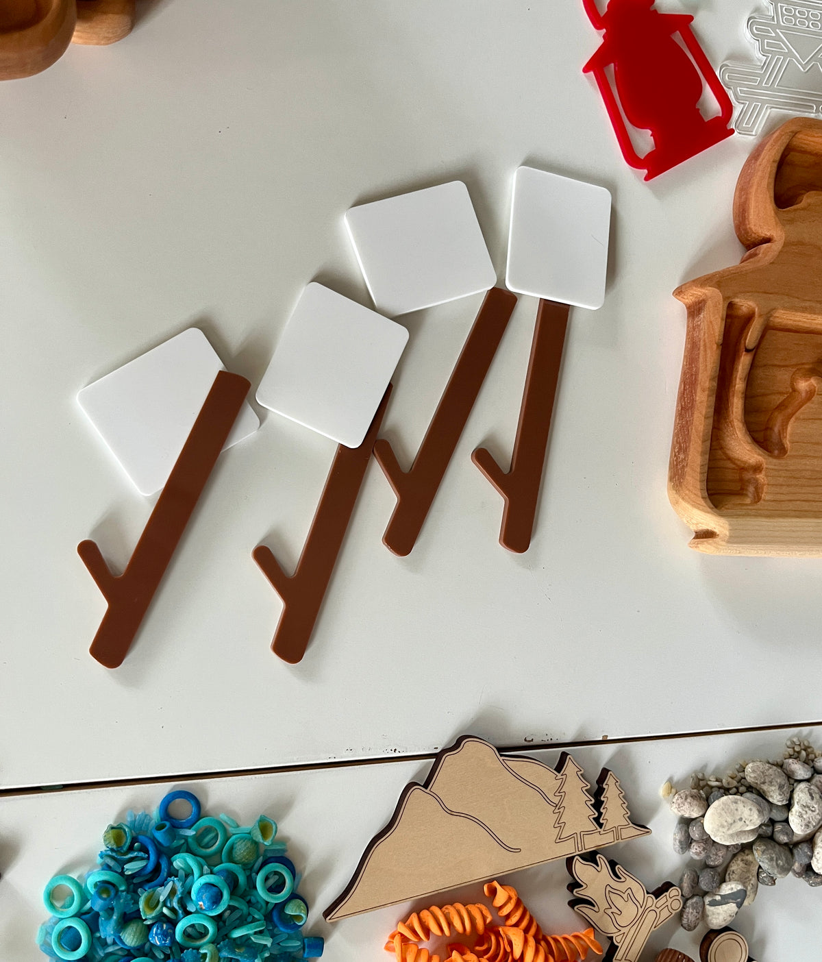 Wooden and plastic play pieces arranged on table including brown branches with white squares, map cutout, blue rings, and orange spiral shapes