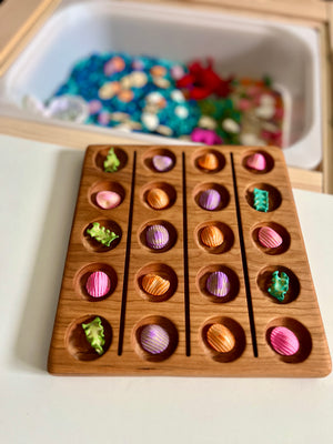 Wooden tray with rows of pink, orange, purple seashell-shaped pieces and green coral-shaped figures on a white surface