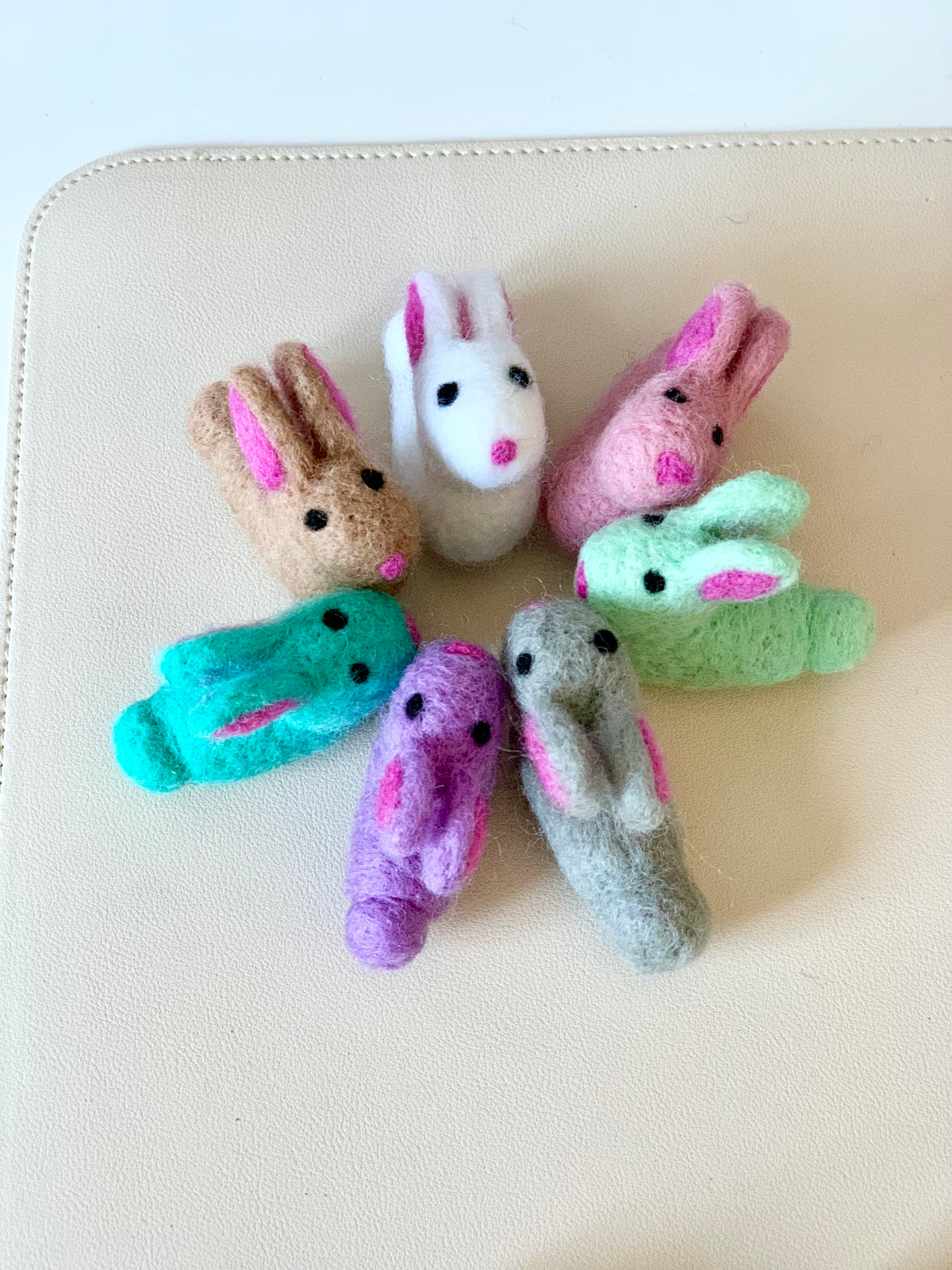 Seven small felt bunny finger puppets in a circle on a light beige surface with various pastel colors