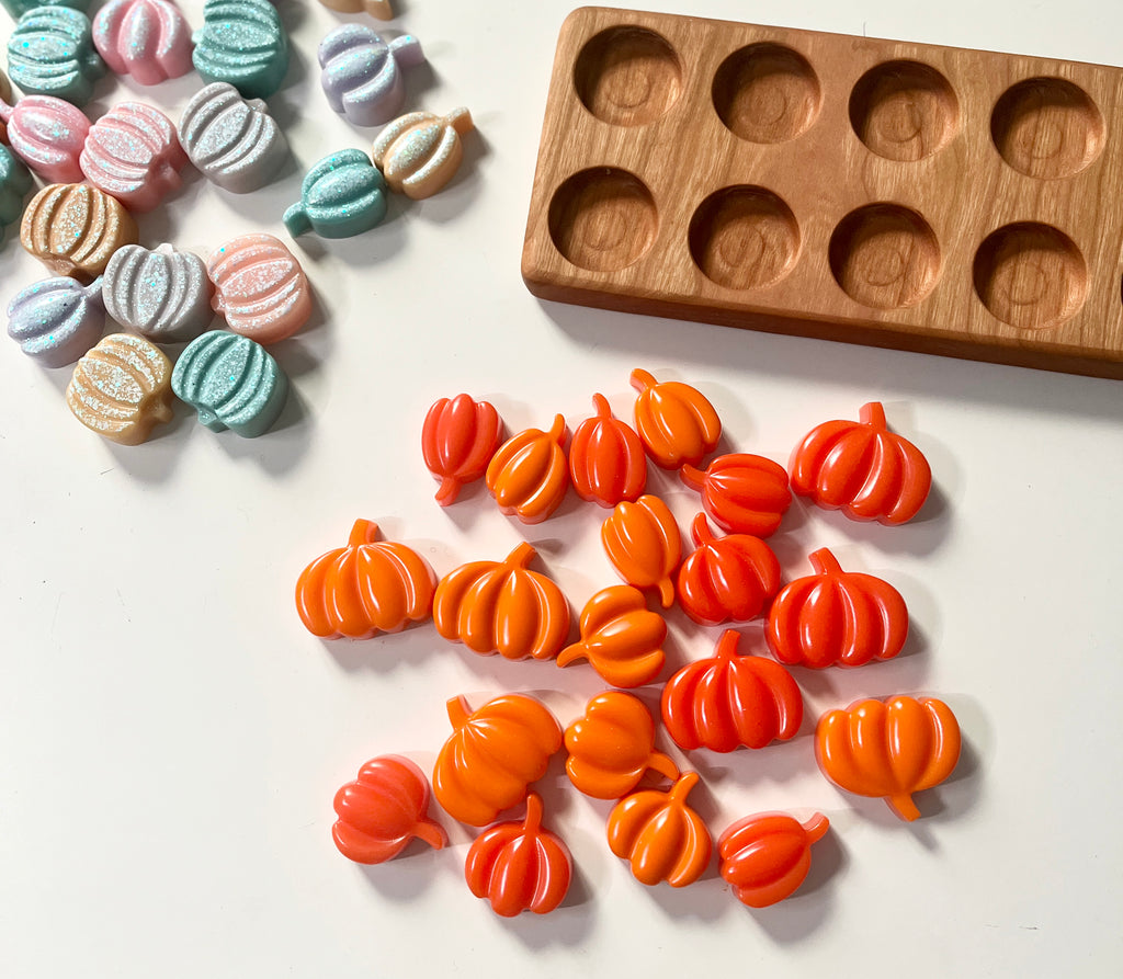 Orange pumpkin-shaped resin toys on a white surface with a wooden ten frame
