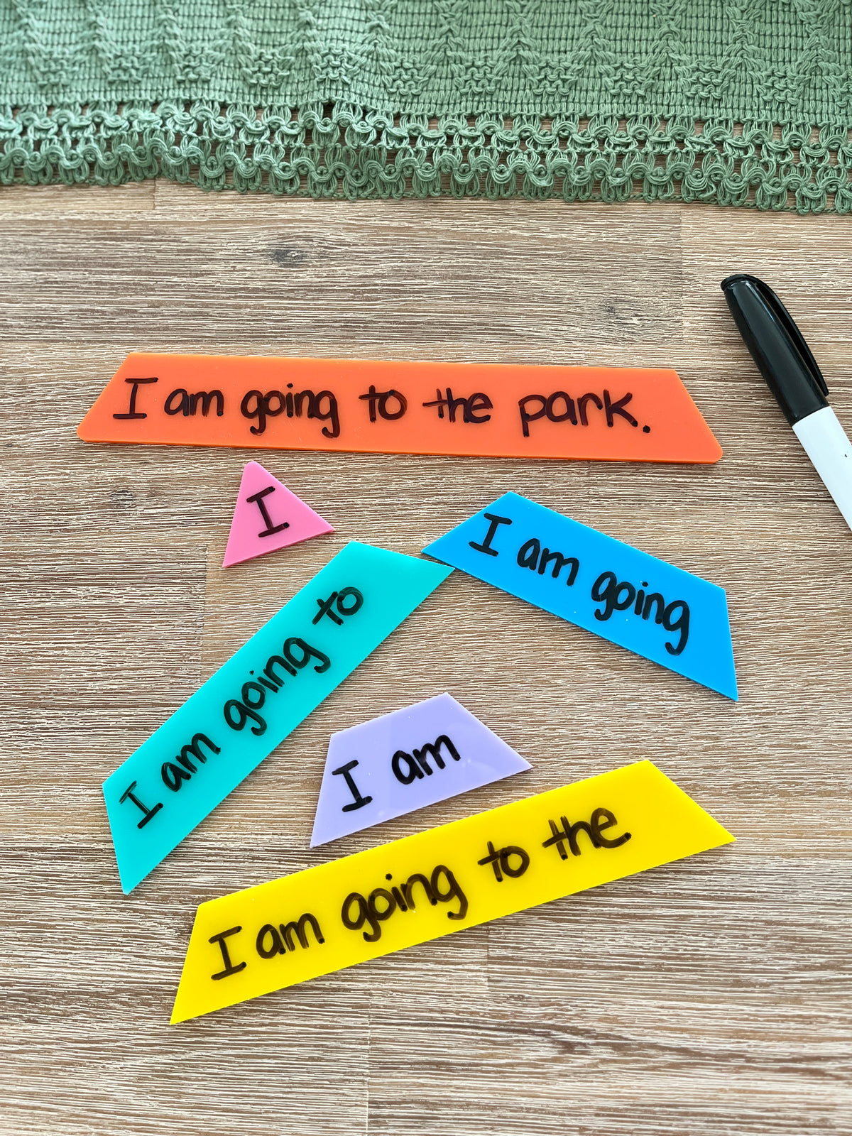 Little Dry Erasable Sentence Building Pyramid; Fluency Triangle pieces in various colors arranged on wood surface with black dry erase marker and green textured fabric, handcrafted homeschool education resources.