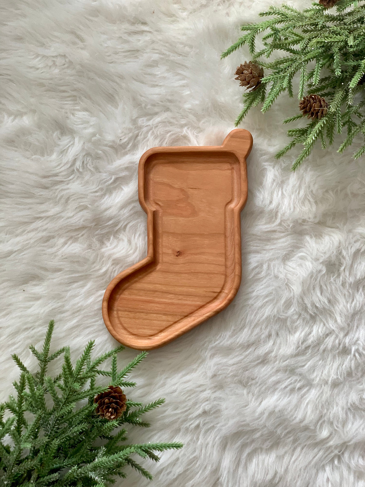 Wooden stocking-shaped sensory tray on white faux fur with green pine branches and pinecones surrounding it