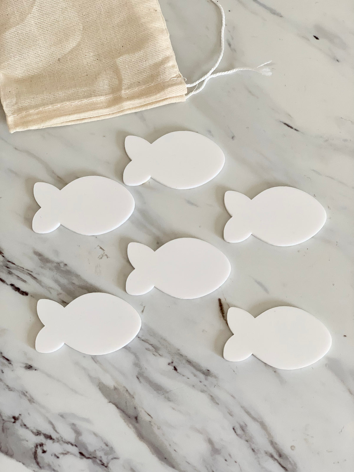 Set of six white fish-shaped dry erase boards with drawstring cotton pouch on marble surface