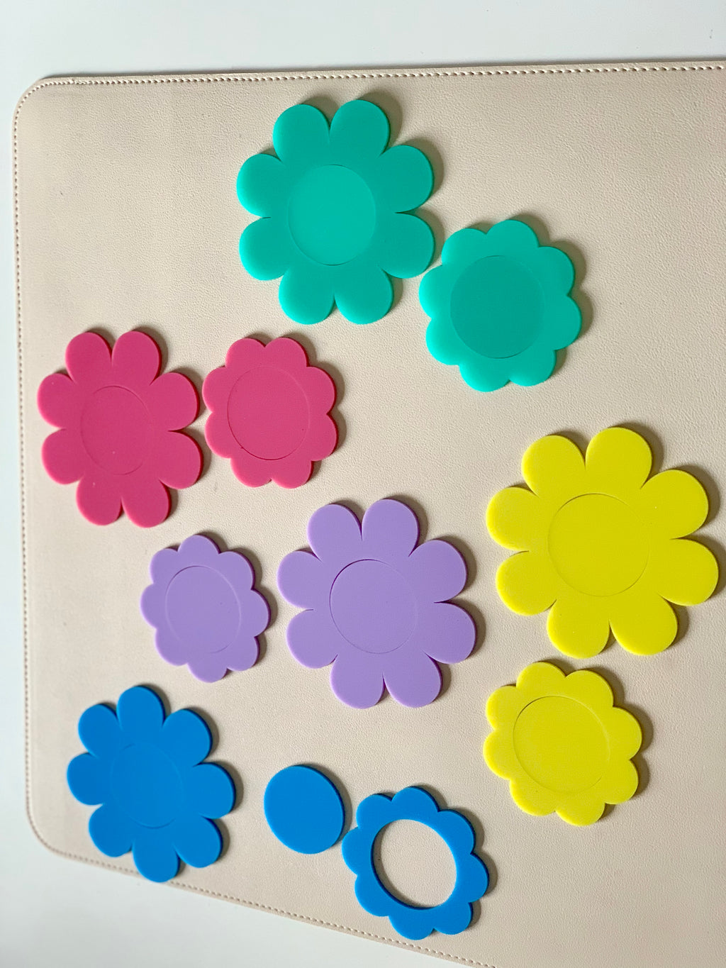 Various colorful flower-shaped plastic pieces and two yellow circular disks arranged on a light surface