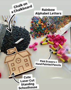 Small rainbow alphabet beads, pink erasers, hand-painted pencil pieces, black chalk on white surface, and wooden schoolhouse cutout