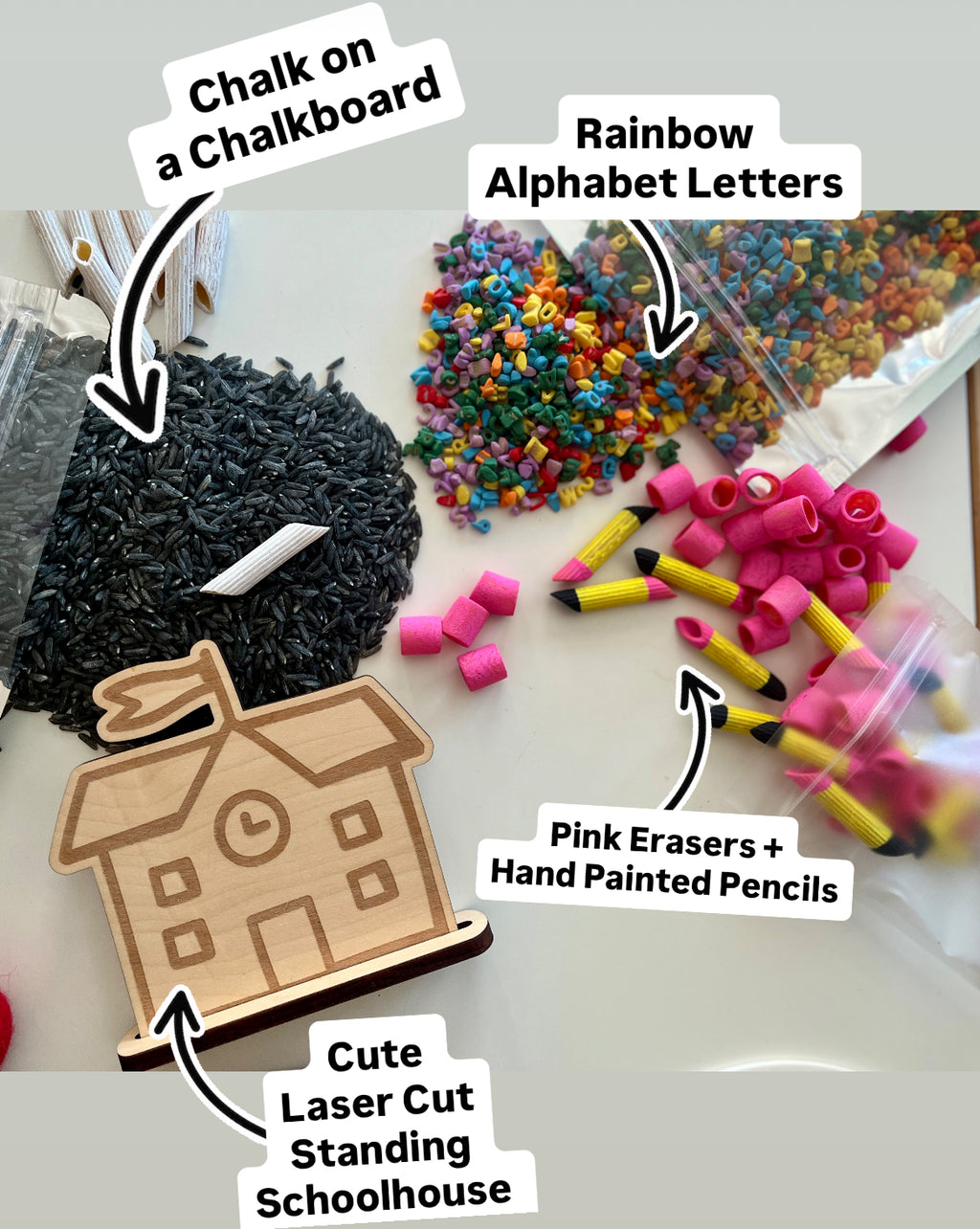Small rainbow alphabet beads, pink erasers, hand-painted pencil pieces, black chalk on white surface, and wooden schoolhouse cutout