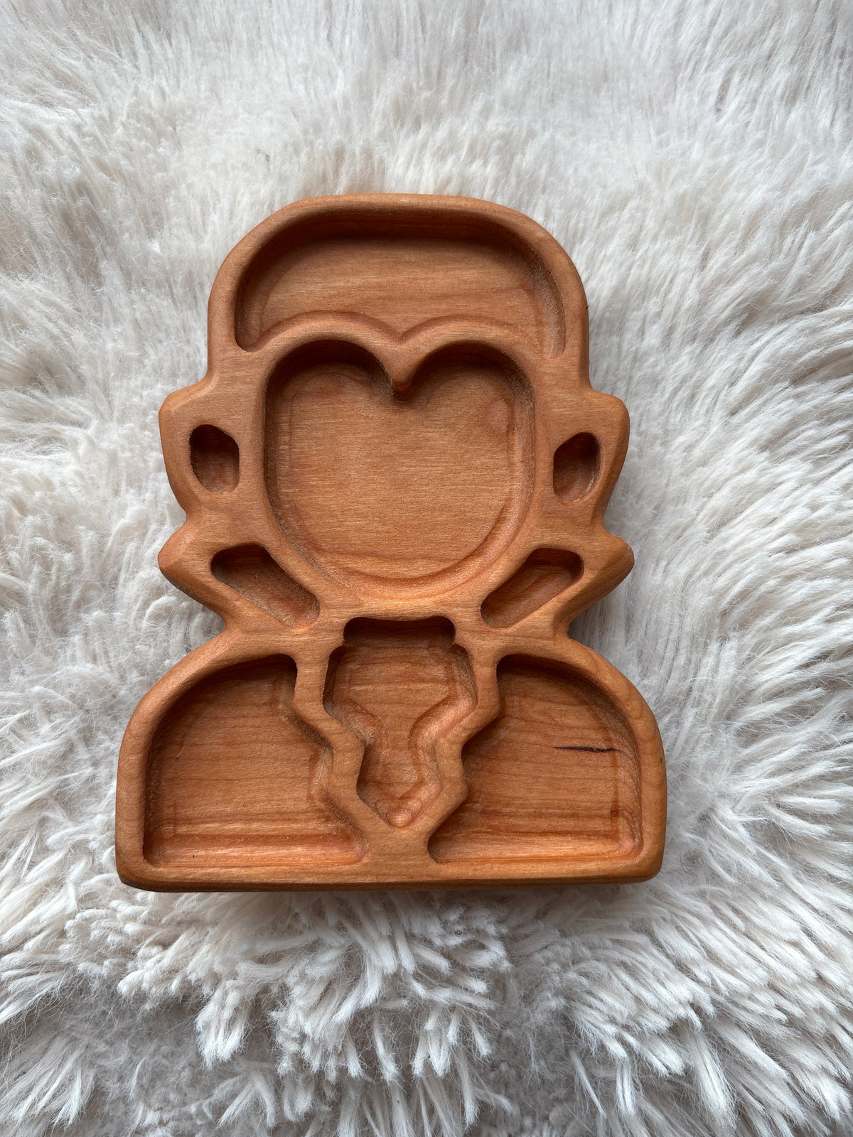 Carved wooden tray in the shape of a stylized person with heart-shaped face indentations on a soft textured surface