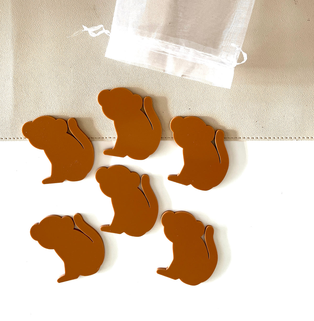 Six brown monkey-shaped pieces arranged near a sheer white drawstring pouch on a light fabric surface